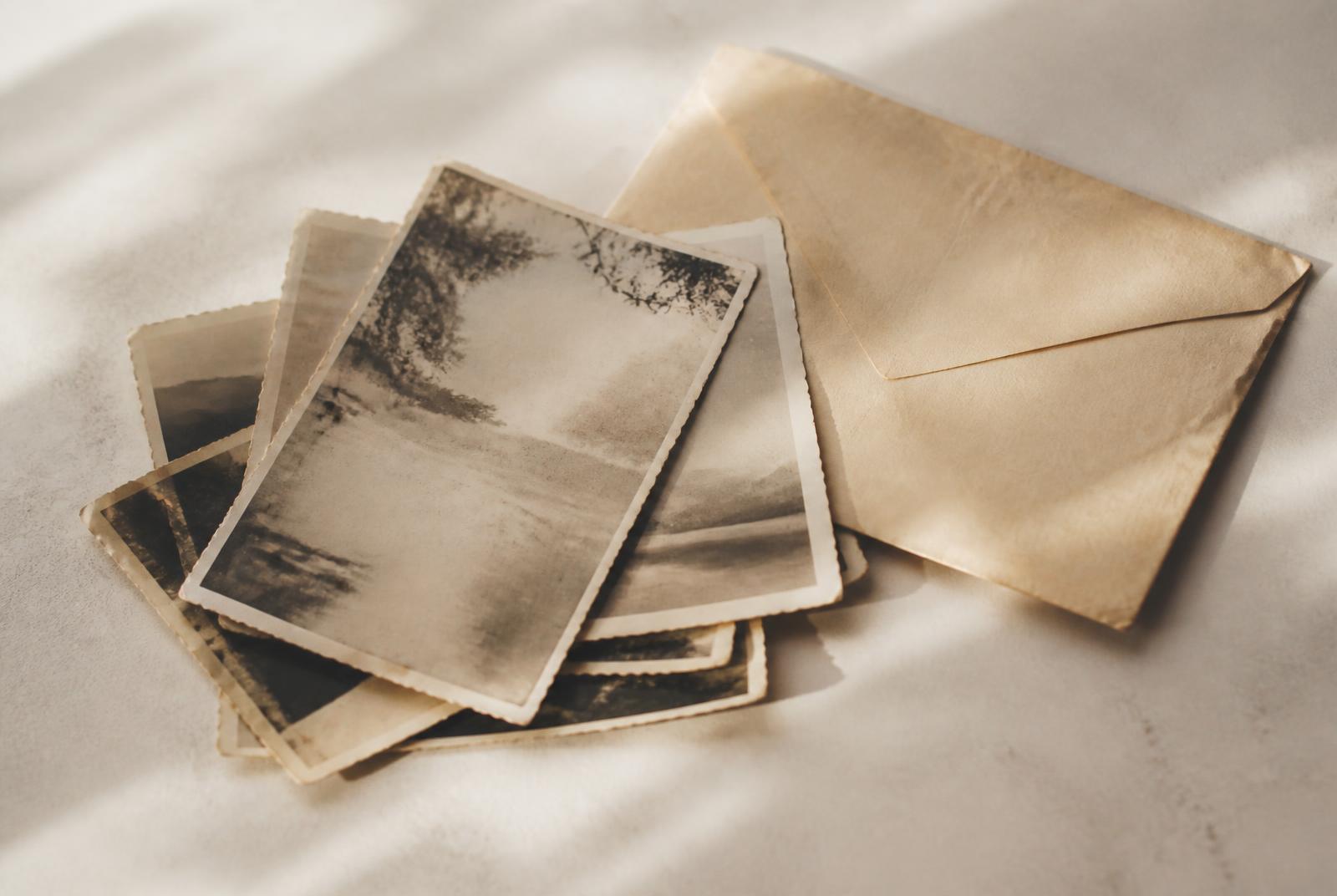 Stack of old faded photographs and a vintage envelope in raking daylight