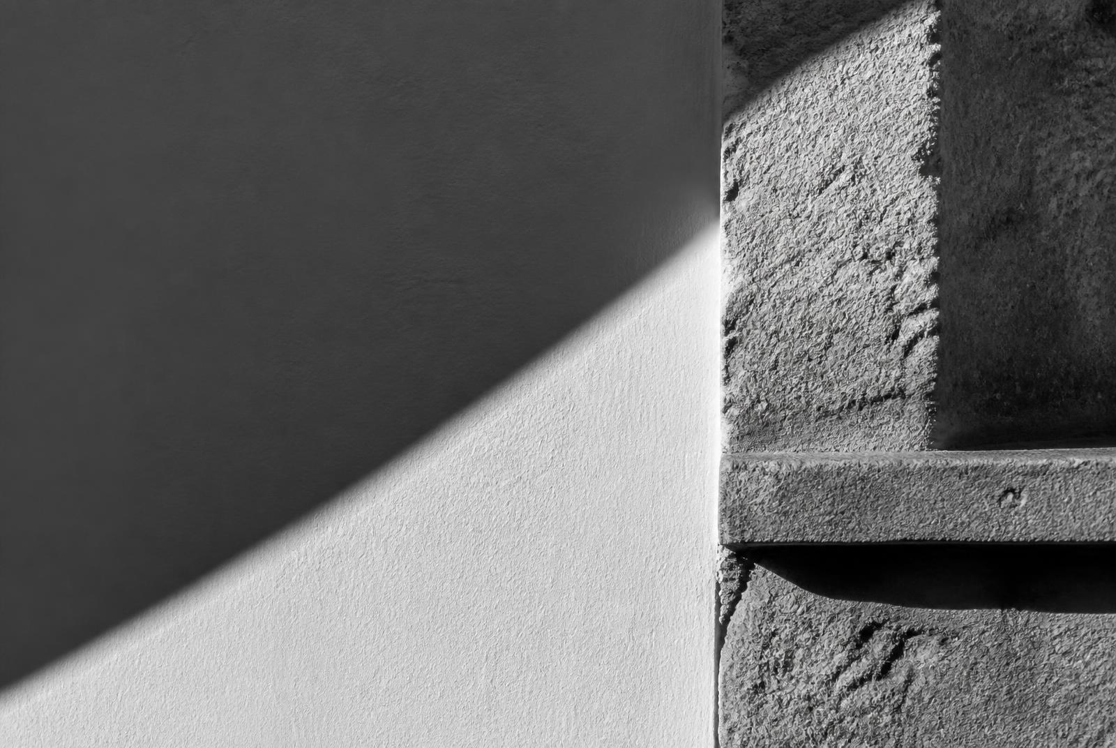 Black and white close-up of a shadow line across a plaster wall meeting stone